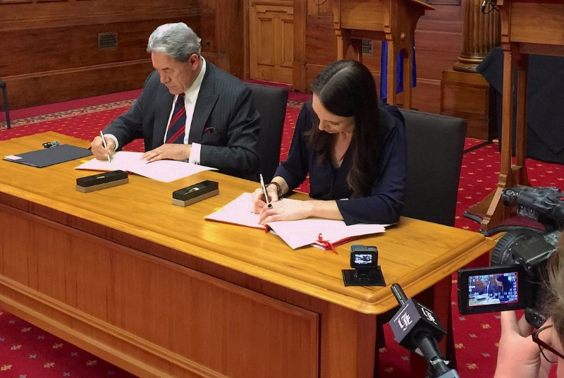 © Reuters. New Zealand Prime Minister-designate Jacinda Ardern signs official documents next to New Zealand First party leader Winston Peters after their meeting in Wellington