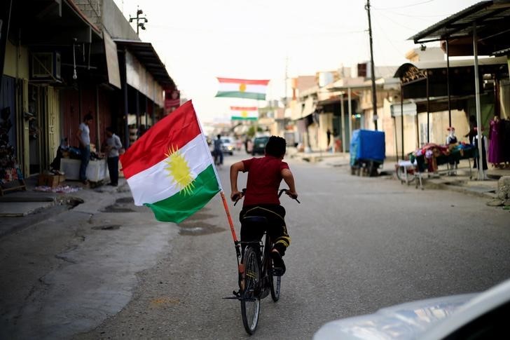 © Reuters. Menino anda em bicicleta com bandeira do Curdistão em Tuz Khurmato, no Iraque