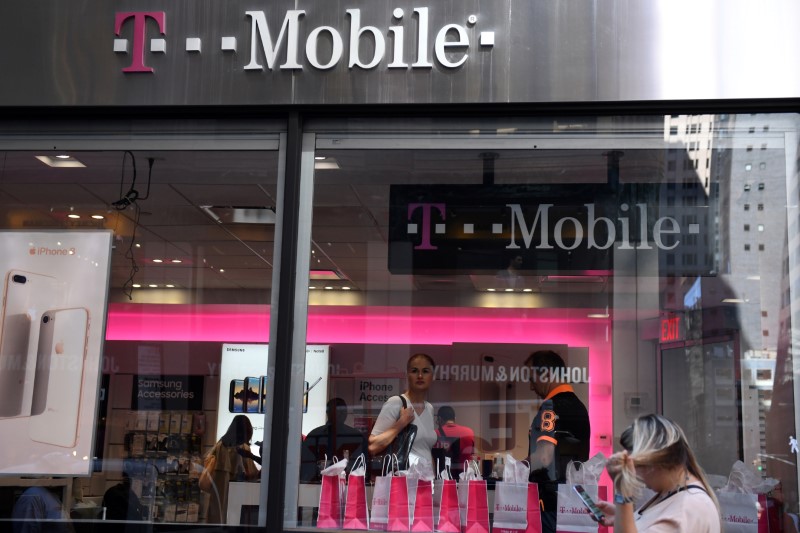 © Reuters. A pedestrian uses her smart phone as she passes a T-Mobile retail store in New York City