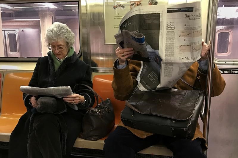 © Reuters. A couple of people ride the subway as they read newspapers as the train pulls into the Times Square stop in Manhattan