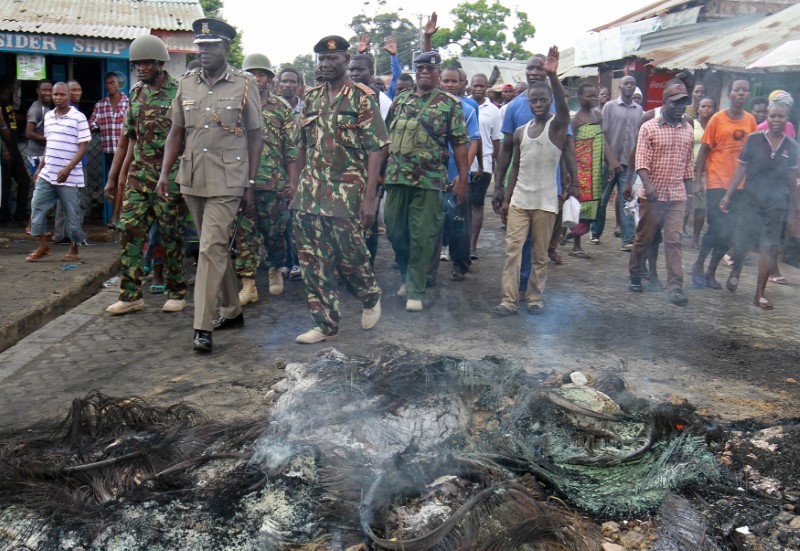 © Reuters. Police officers walk past burnt tires that were set on fire by protesters against a presidential election re-run in Bangladesh area in Changamwe, Mombasa