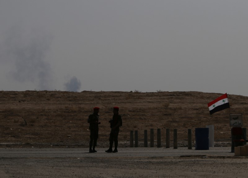 © Reuters. Smoke rises as Syrian army soldiers stand near a checkpoint in Deir al-Zor