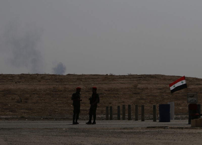 © Reuters. FILE PHOTO: Smoke rises as Syrian army soldiers stand near a checkpoint in Deir al-Zor