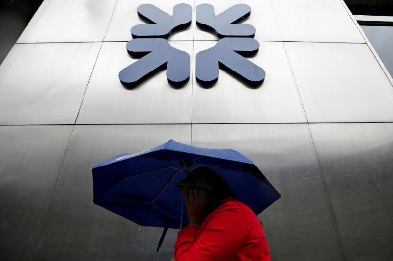 © Reuters. FILE PHOTO: A woman shelters under an umbrella as she walks past a branch of RBS in the City of London