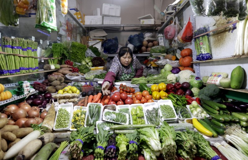 © Reuters. FILE PHOTO: A vendor reaches out for vegetables at her shop in a market in Beijing