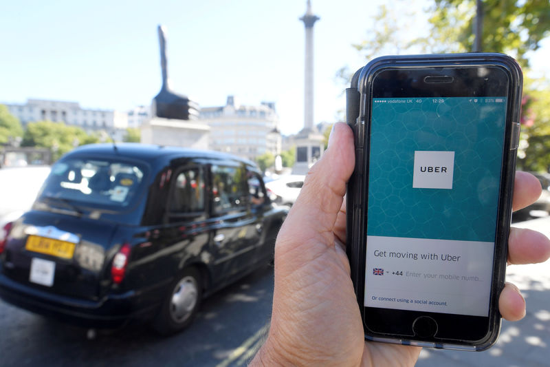 © Reuters. FILE PHOTO: A photo illustration shows a London taxi passing as the Uber app logo is displayed on a mobile telephone, as it is held up for a posed photograph in central London