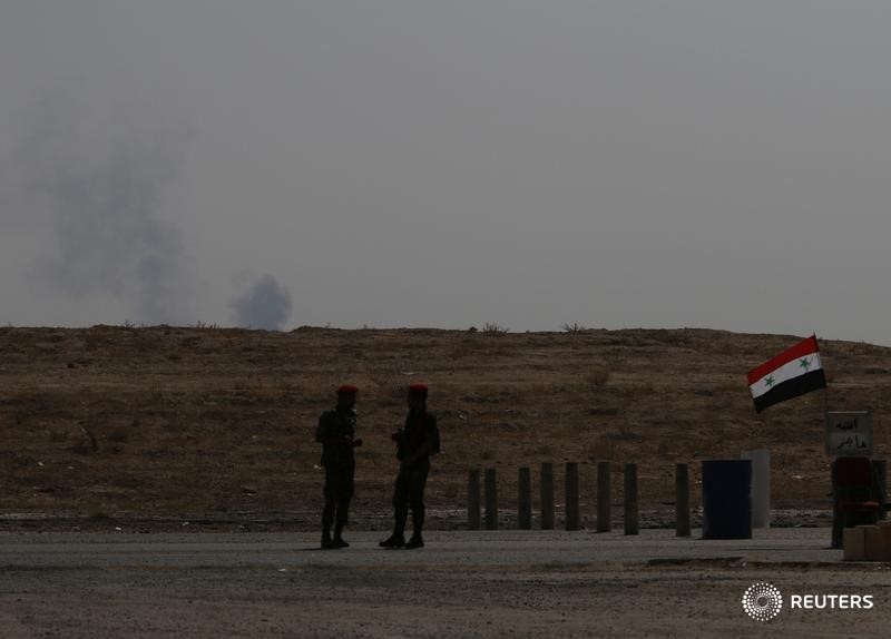 © Reuters. Smoke rises as Syrian army soldiers stand near a checkpoint in Deir al-Zor