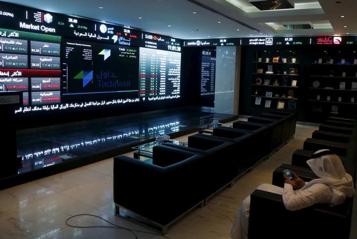 © Reuters. FILE PHOTO - A trader uses his mobile as he monitors screens displaying stock information at the Saudi Stock Exchange (Tadawul) in Riyadh
