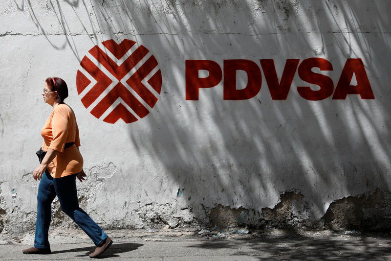 © Reuters. A woman walks past a mural with the corporate logo of the state oil company PDVSA in Caracas