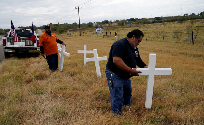 © Reuters. Chris Alcala and Albert Zapata erect a line of crosses along the highway on the outskirts of the town where the shooting took place at the First Baptist Church of Sutherland Springs