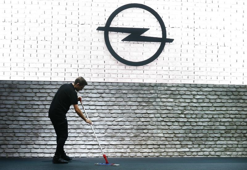 © Reuters. Man cleans the floor near a wall with an Opel logo on it during the Frankfurt Motor Show (IAA) in Frankfurt