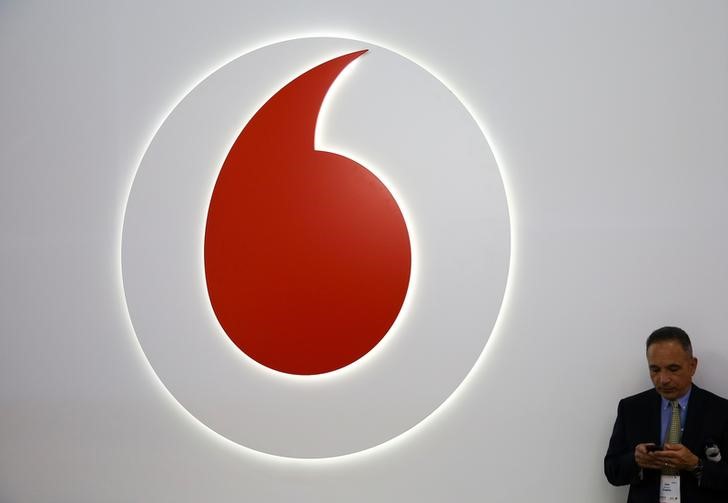 © Reuters. A man looks at his phone next to a Vodafone logo at the Mobile World Congress in Barcelona