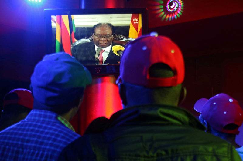 © Reuters. People watch as Zimbabwean President Robert Mugabe addresses the nation on television, at a bar in Harare