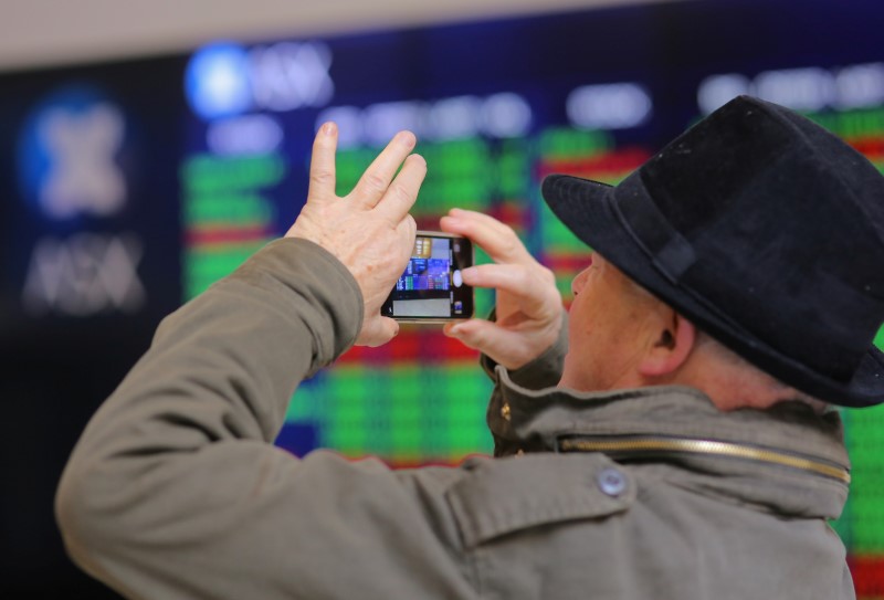 © Reuters. An investor takes a photograph using his phone as he stands in front a board displaying stock prices at the Australian Securities Exchange in Sydney