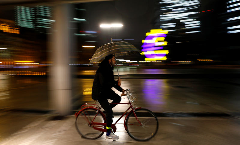 © Reuters. Cyclist holding an umbrella passes by the euro sign in Frankfurt