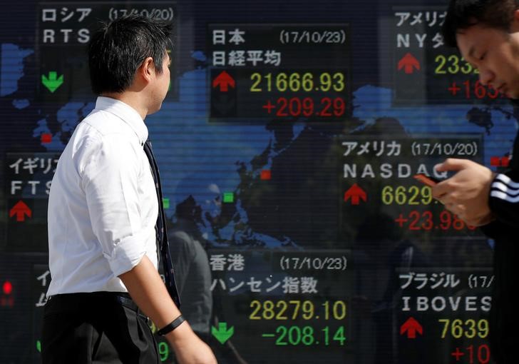 © Reuters. Passersby walk past an electronic board showing market indices outside a brokerage in Tokyo
