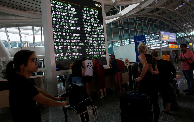 © Reuters. Passengers stand near the flight information board after Indonesian and regional authorities heightened flight warnings, following the eruption of Bali's Mount Agung volcano at Ngurah Rai International airpot in Bali