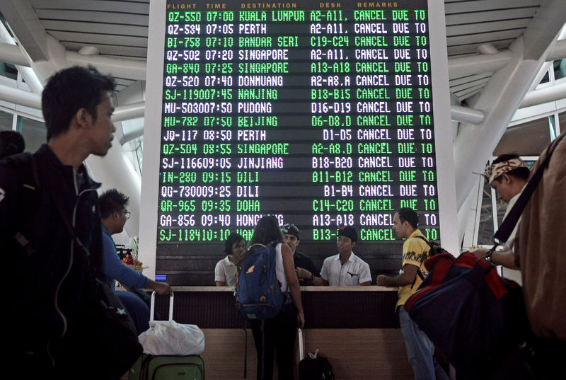 © Reuters. Passageiros passam por tela com informações sobre voos cancelados no aeroporto de Ngurah Rai, em Bali