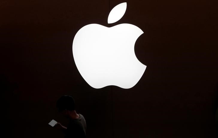 © Reuters. A man looks at the screen of his mobile phone in front of an Apple logo outside its store in Shanghai