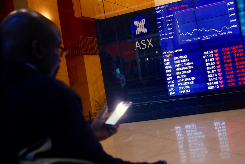 © Reuters. An investor uses his phone as he sits in front of a board displaying stock prices at the Australian Securities Exchange in Sydney
