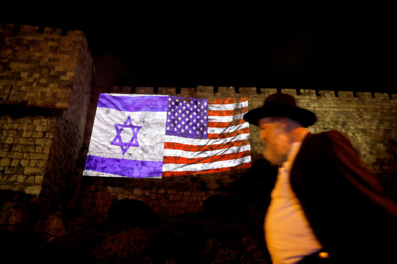 © Reuters. Man walks by as the Israeli national flag and an American one are projected on a part of the walls surrounding Jerusalem's Old City