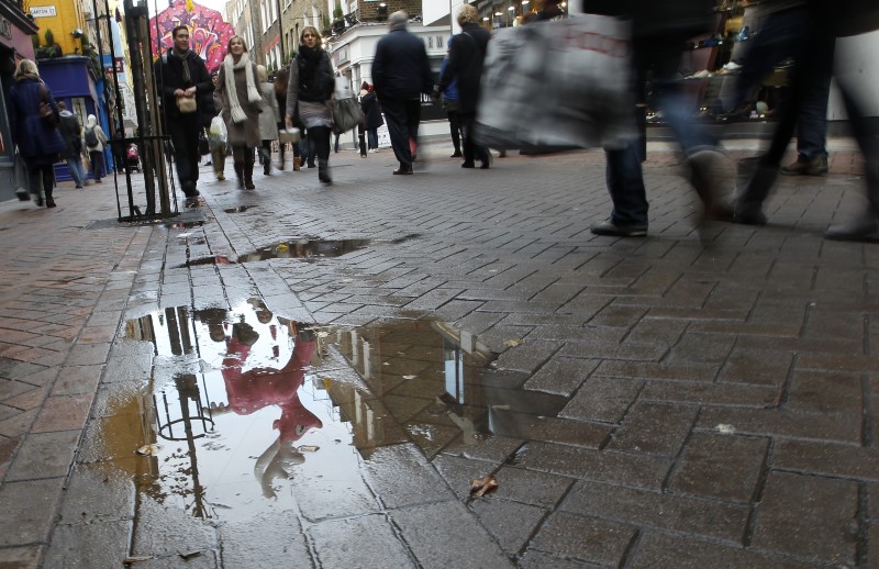 © Reuters. Shoppers walk past a Christmas decoration reflected in a puddle in a street in London