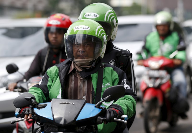 © Reuters. FILE PHOTO - Driver and passenger ride on a motorbike, part of the Go-Jek ride-hailing service, on a busy street in central Jakarta