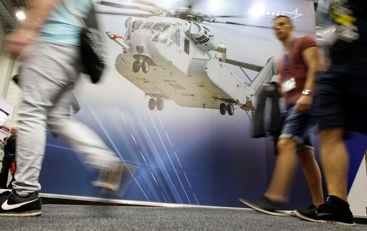 © Reuters. Visitors walks past a picture of a CH-53 helicopter at the booth of Sikorsky - Lockheed Martin company on the ILA Berlin Air Show in Schoenefeld