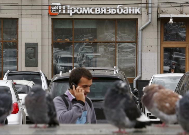 © Reuters. Man speaks on the phone near pigeons, with a branch of Promsvyazbank seen in the background, in Moscow