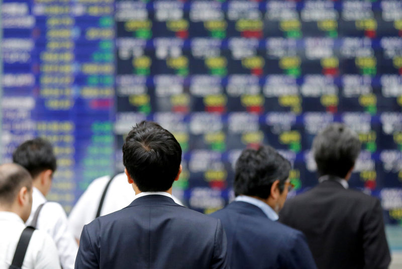 © Reuters. FILE PHOTO: People walk past an electronic stock quotation board outside a brokerage in Tokyo