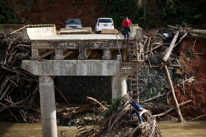 © Reuters. A woman looks as her husband climbs down a ladder at a partially destroyed bridge, after Hurricane Maria hit the area in September, in Utuado