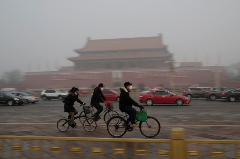 © Reuters. People wearing masks cycle past Tiananmen Gate during the smog in Beijing