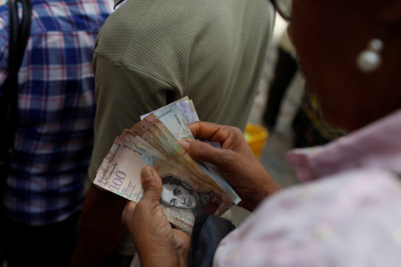 © Reuters. FILE PHOTO: A woman counts Venezuelan bolivar notes at a vegetable street market in Caracas