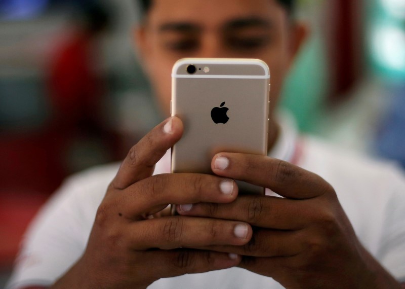 © Reuters. FILE PHOTO - A salesman checks a customer's iPhone at a mobile phone store in New Delhi