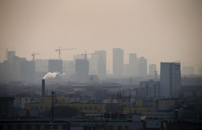 © Reuters. FILE PHOTO: File photo of smoke rising from a chimney among houses as new high-rise residential buildings are seen under construction on a hazy day in the city centre of Tangshan