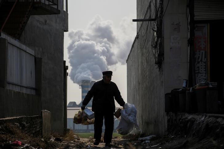 © Reuters. A man collects recyclables from an alley as smoke billows from the chimney of a factory in rural Gaoyi county near Shijiazhuang