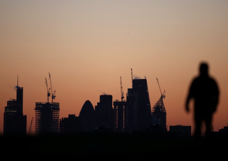 © Reuters. A man walks accross Primrose Hill as dawn breaks behind construction cranes in the City of London