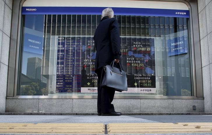 © Reuters. FILE PHOTO - A pedestrian stands to look at an electronic board showing the stock market indices of various countries outside a brokerage in Tokyo