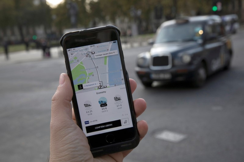 © Reuters. FILE PHOTO: A photo illustration shows the Uber app on a mobile telephone, as it is held up for a posed photograph, with a London Taxi in the background, in London