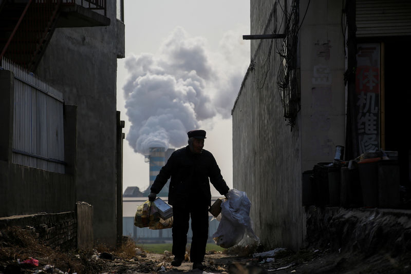 © Reuters. FILE PHOTO: Man collects recyclables from an alley as smoke billows from the chimney of a factory in rural Gaoyi county near Shijiazhuang