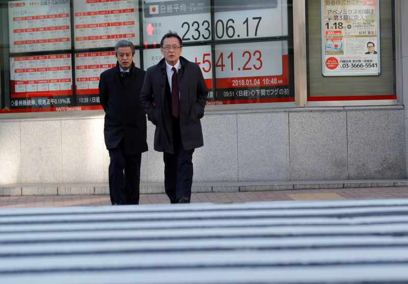 © Reuters. Pedestrians walk past an electronic board displaying the Nikkei average outside a brokerage in Tokyo