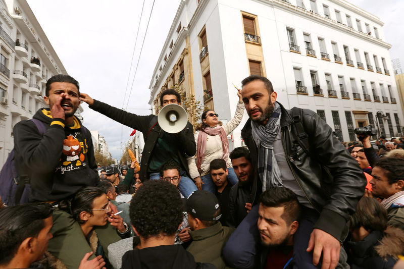 © Reuters. Demonstrating graduate students shout slogans, as riot police stand guard, during protests against rising prices and tax increases, in Tunis