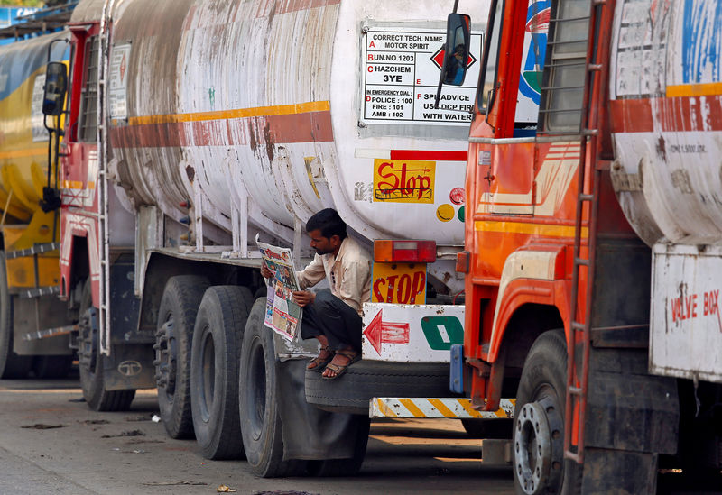 © Reuters. FILE PHOTO: A driver reads a newspaper as he sits on a spare tire attached to a parked oil tanker at a truck terminal in Mumbai