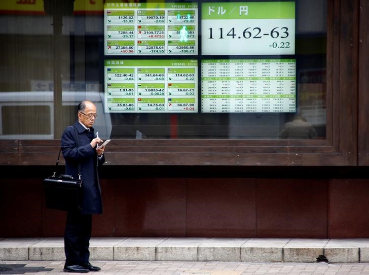 © Reuters. FILE PHOTO-A man stands in front of electronic boards showing stock prices and exchange rate between Japanese Yen and U.S dollar outside a brokerage in Tokyo