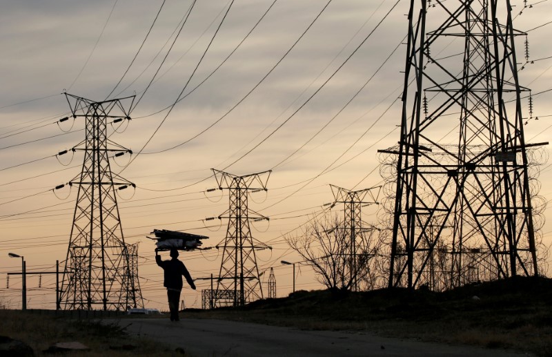 © Reuters. A woman carries fire wood on her head as she walks below Eskom's Elecricity pylons in Soweto,South Africa