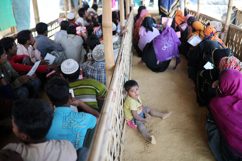 © Reuters. A Rohingya child sits on the floor while his mother waits in a queue to collect aid supplies in Kutupalong refugee camp in Cox's Bazar