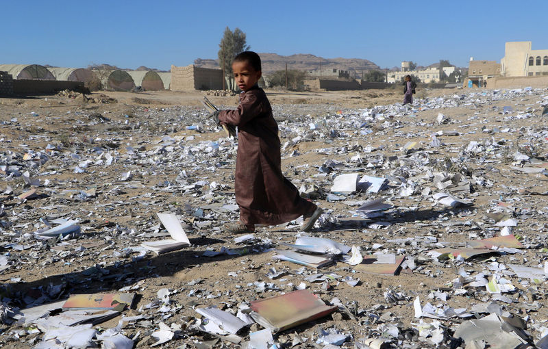 © Reuters. Boy holds a book as he walks on books scattered on the ground after an air strike hit a school book storage building in the northwestern city of Saada
