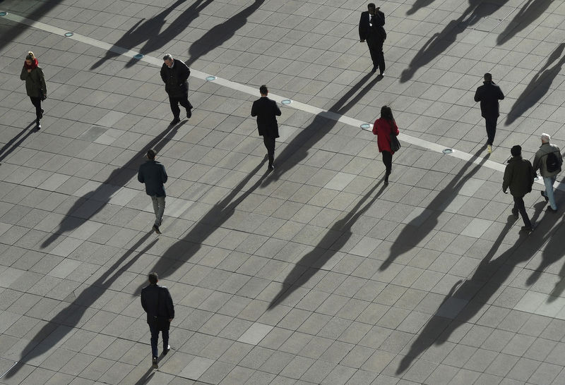 © Reuters. People cast long shadows in the winter sunlight as they walk accross a plaza in the Canary Wharf financial district of London