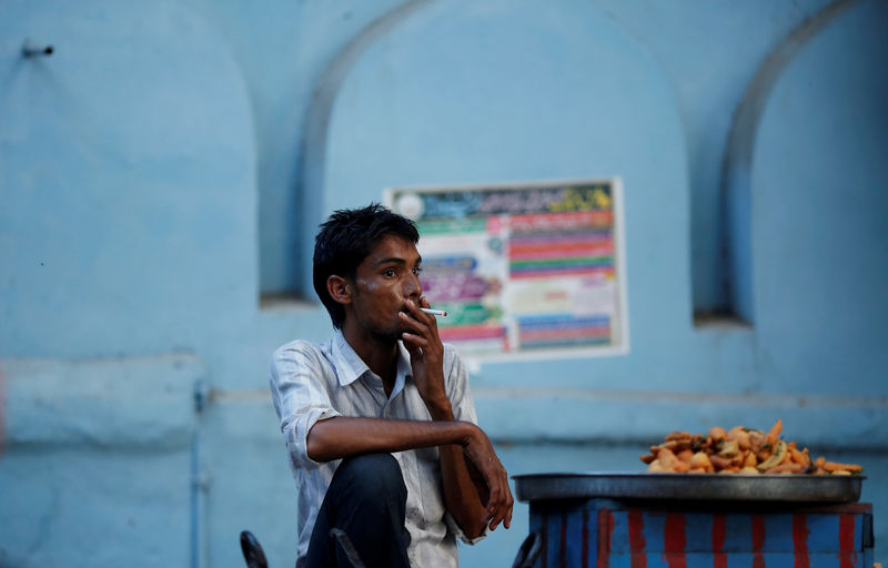 © Reuters. FILE PHOTO: A snack vendor smokes a cigarette as he waits for customers on a street in New Delhi