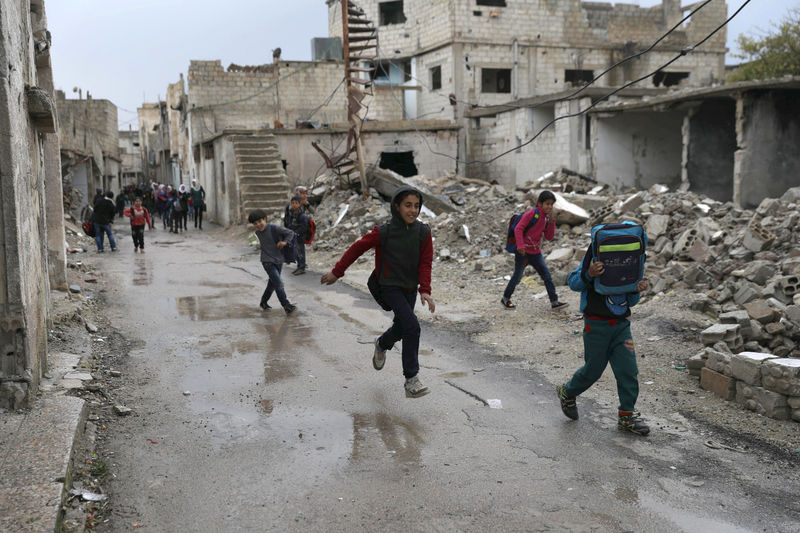 © Reuters. Estudantes passam perto de prédios destruídos na cidade síria de Deraa